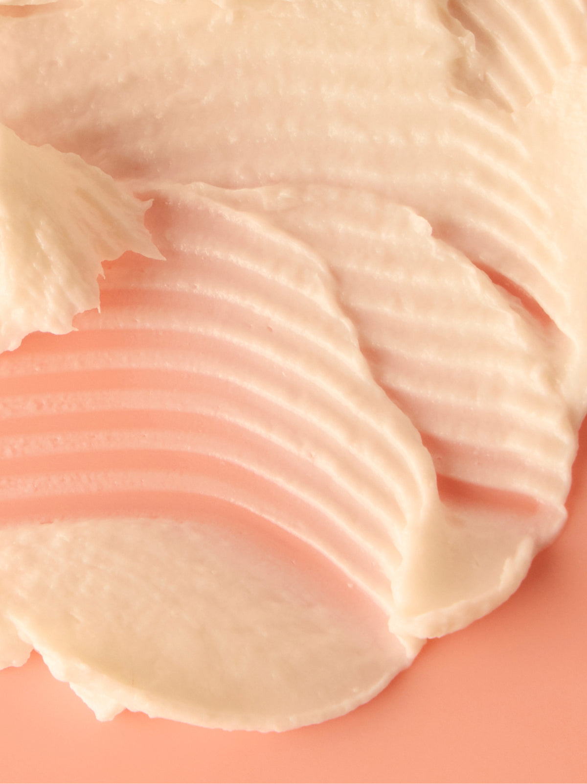 Close up of peach and ivory skincare cream swatches with soft ridged texture layered on a warm coral background from Go To Skincare