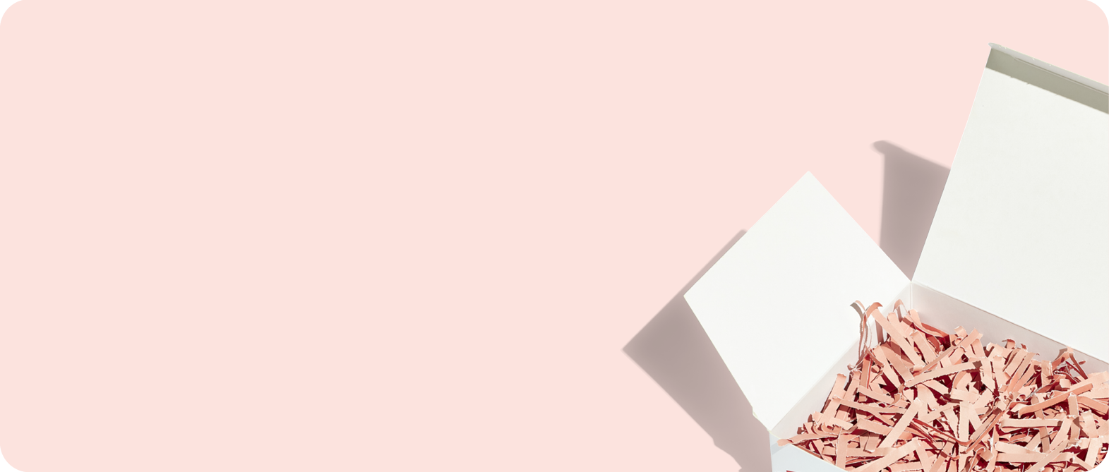 A white box with its lid open sits in the lower right corner on a pale pink background, filled with pink paper shreds.