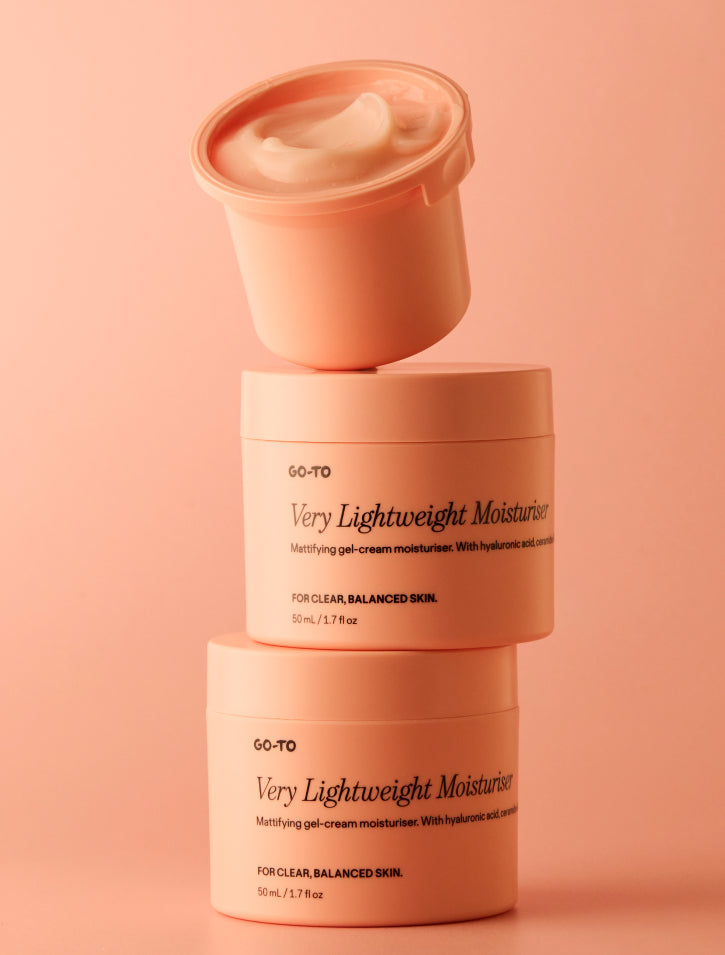 Three Go-To Very Lightweight Moisturiser jars stacked, the top one open showing white gel-cream texture, against a peach background.