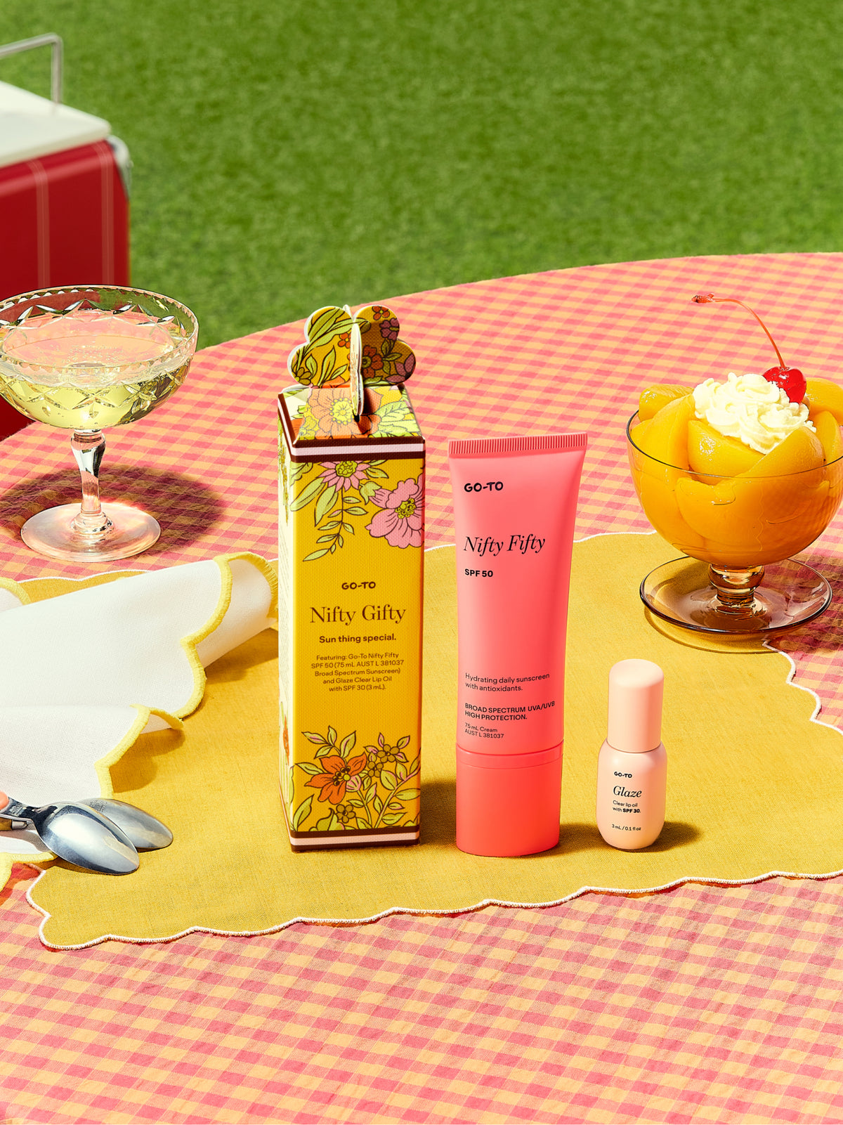Go To Skincare Nifty Gifty floral gift set with a pink sunscreen tube and mini skincare bottle on a colorful picnic table with drinks and dessert